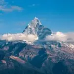 Breathtaking view of a snow-covered mountain peak surrounded by clouds during sunrise.